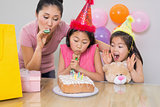 Girls and mother blowing noisemakers at a birthday party