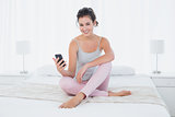 Smiling woman sitting with mobile phone in bed