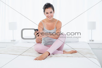 Smiling woman sitting with mobile phone in bed