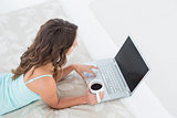 Woman using laptop with coffee cup in bed