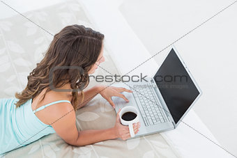 Woman using laptop with coffee cup in bed
