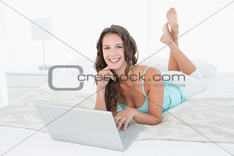 Relaxed smiling young woman using laptop in bed