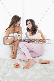 Cheerful female friends with coffee cups in bed