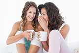 Relaxed female friends with coffee cups gossiping in bed