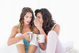 Relaxed female friends with coffee cups gossiping in bed