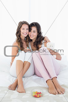 Cheerful female friends sitting on bed with arm around