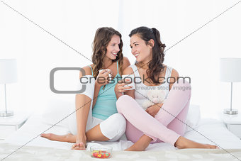 Young female friends with coffee cups in bed