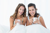 Smiling female friends with coffee cups in bed