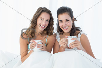 Smiling female friends with coffee cups in bed