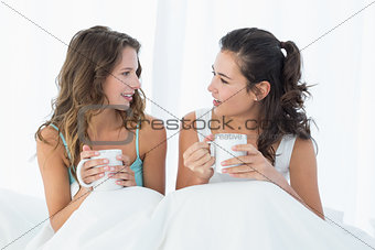 Female friends with coffee cups chatting in bed