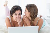 Relaxed female friends with laptop gossiping in bed