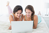 Happy relaxed female friends using laptop in bed