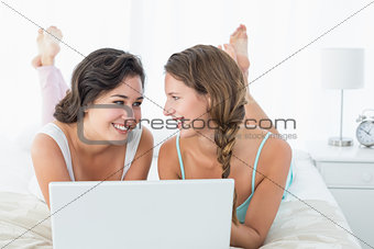Happy relaxed female friends using laptop in bed