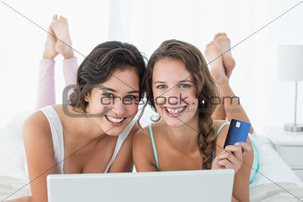 Happy relaxed friends doing online shopping in bed