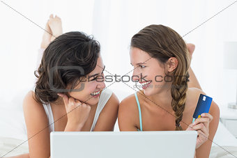 Relaxed friends doing online shopping in bed
