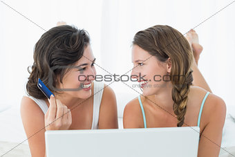 Female friends doing online shopping in bed