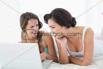 Relaxed female friends using laptop in bed