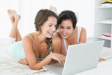 Relaxed smiling friends using laptop in bed