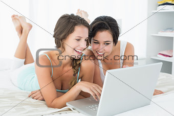 Relaxed smiling friends using laptop in bed