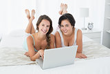 Female friends using laptop in bed