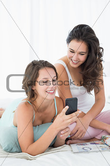 Female friends reading text message in bed