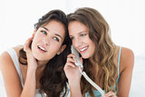 Relaxed young female friends using phone in bed