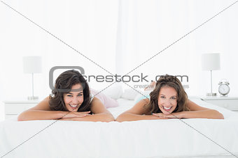 Two smiling young female friends lying in bed
