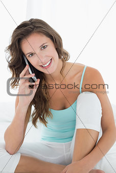 Smiling woman in tank top using mobile phone in bed