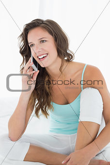 Woman in tank top using mobile phone in bed