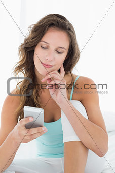 Smiling woman looking at mobile phone in bed