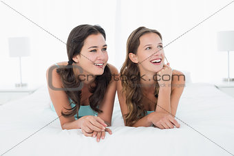 Smiling young female friends lying in bed
