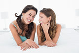 Smiling young female friends lying in bed