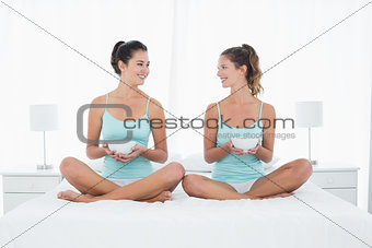 Female friends with bowls sitting on bed