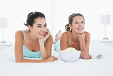 Smiling female friends with popcorn bowl lying in bed