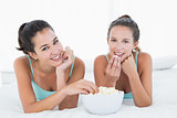 Smiling female friends eating popcorn in bed