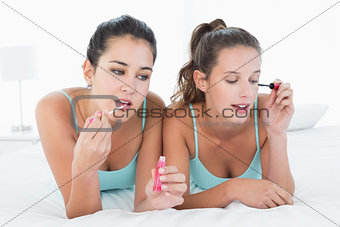 Female friends applying make-up in bed