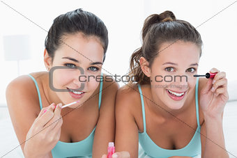 Two young female friends applying make-up in bed