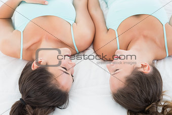 Female friends in teal tank tops lying in bed