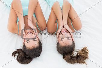 Two female friends in teal tank tops lying in bed