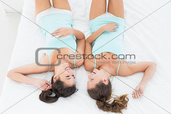 Two female friends in teal tank tops lying in bed