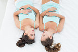 Two female friends in teal tank tops sleeping in bed