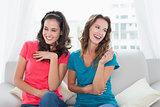 Cheerful young female friends sitting on sofa at home
