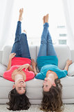 Smiling friends lying on sofa with legs in the air at home