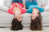 female friends lying upside down on sofa at home