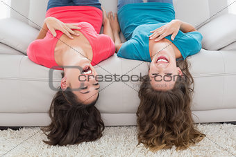 Cheerful friends lying upside down on sofa at home