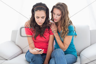 Upset female friends reading text message at home