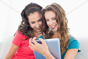 Two smiling young female friends using digital tablet