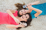 Two female friends lying on rug and text messaging