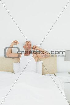 Mature smiling man stretching arms in bed