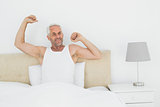 Mature smiling man stretching arms in bed